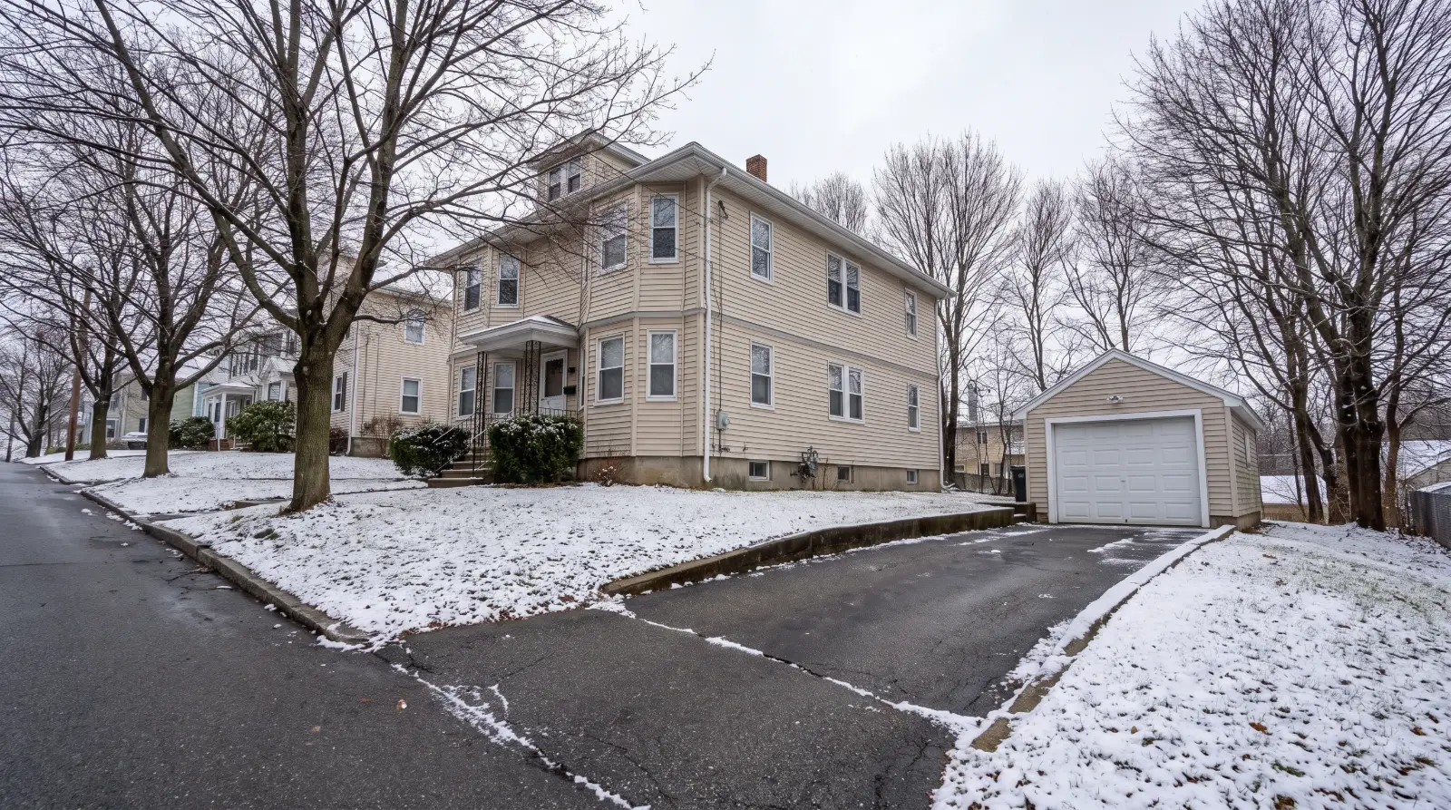Two-family house with a detached garage at the end of a snowy driveway